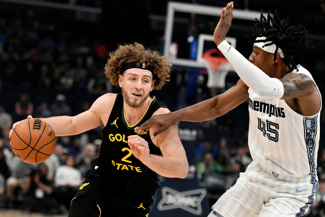 A Golden State player with curly hair drives past a Memphis defender wearing white, both focused intensely as they compete near the basket.